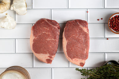 Two grass fed strip steaks on tile background