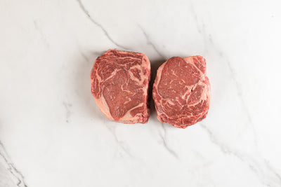 Two grass-fed boneless rib eye steaks on marble background